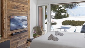 A hotel room with a wooden wall, a flat-screen TV, a bed with towels, and a view of a snowy landscape. - Studio rénové et élégant en plein centre (Crans-Montana)