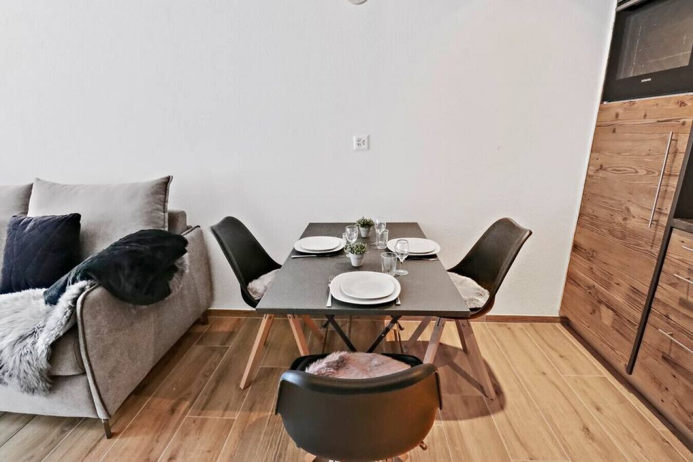 Ein gemütlicher Wohnbereich mit Esstisch für zwei Personen, einer Couch mit Felldecke und Holzboden.