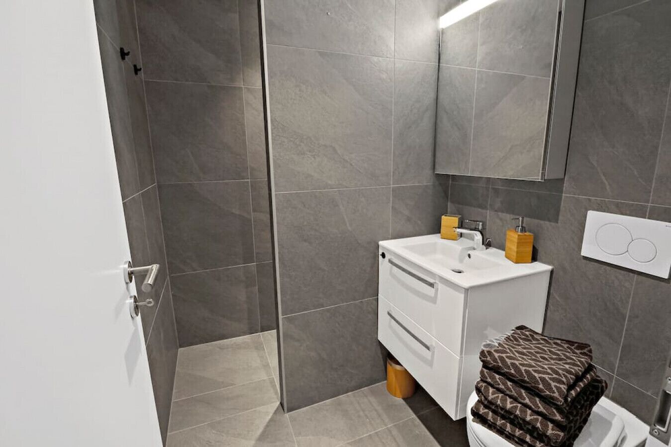 Ein modernes Badezimmer mit grauen Fliesen, einem weißen Waschbecken und einem Spiegel darüber.