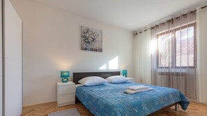 Une chambre à coucher avec un lit, deux tables de chevet, une commode, un tableau accroché au mur et une fenêtre avec des rideaux.