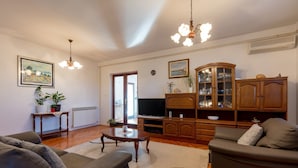 Un salon comprenant un ensemble de canapés, une table basse, un téléviseur, des meubles en bois et un lustre.