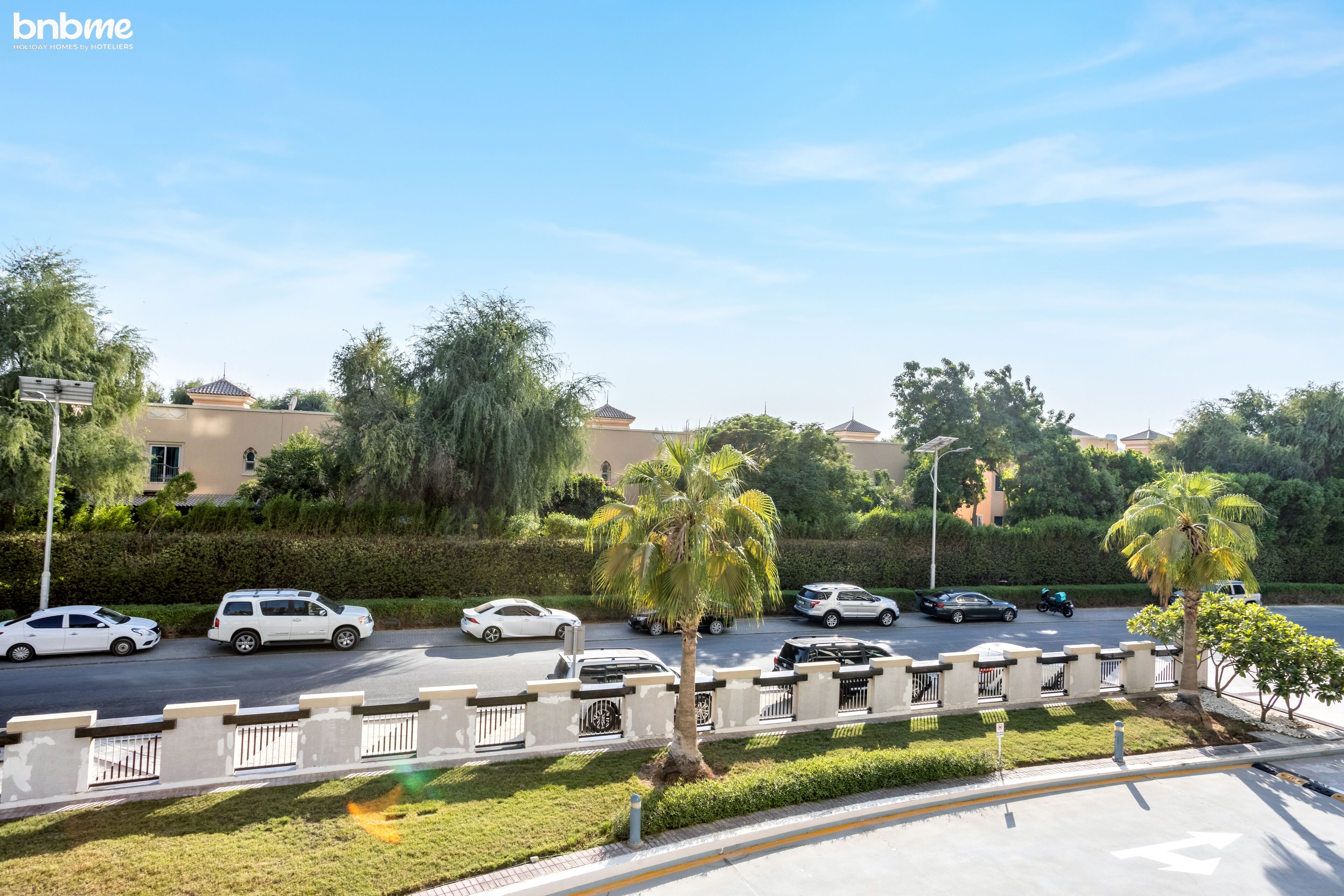 A street view with parked cars, palm trees, and buildings in the background.