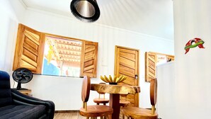 Een eethoek met een houten tafel en stoelen, een ventilator en uitzicht buiten door een raam.