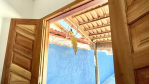 Een open houten deur die leidt naar een kamer met een blauwe muur en een betegeld plafond.