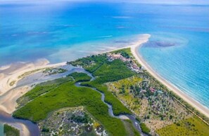 Eine Luftaufnahme einer Küstenlandschaft mit einem sich schlängelnden Fluss, einem Strand und einer kleinen Siedlung.