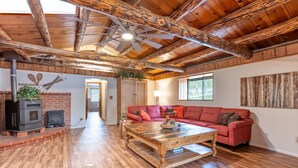 Uma sala de estar espaçosa com teto de madeira, um sofá vermelho, uma mesa de centro de madeira e uma lareira com fogão a lenha.