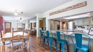 Uma cozinha ampla com uma mesa de jantar de madeira, banquetas azuis e uma placa pendurada acima do balcão.