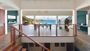 Un balcón amplio con vistas al mar, una zona de comedor con sillas y una escalera que sube a un nivel superior.