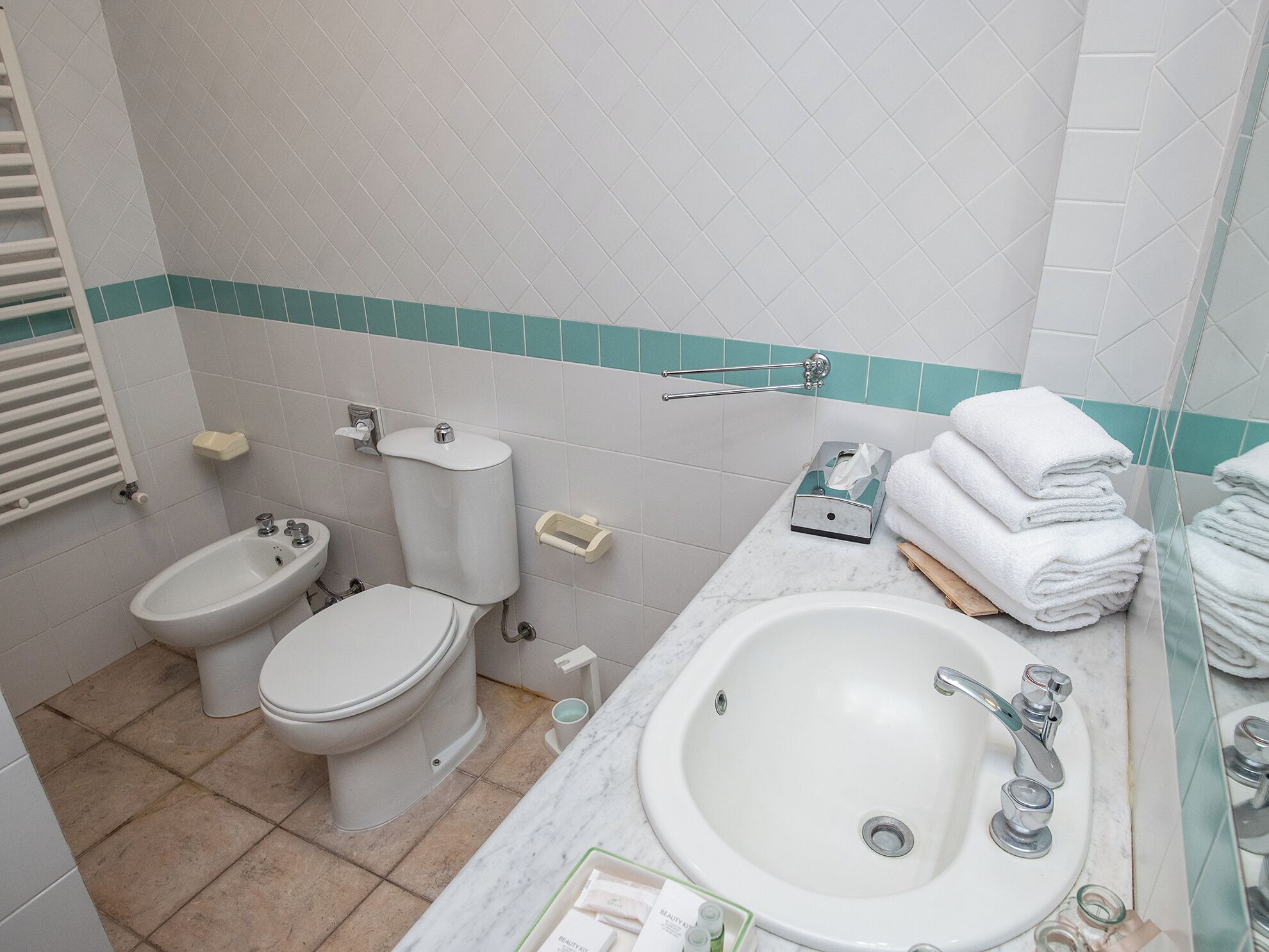 A bathroom with a toilet, bidet, sink, and a towel rack.