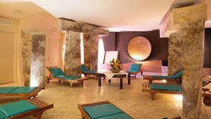 Un área de spa con tumbonas de madera, una mesa central con un florero y un adorno circular grande en la pared.