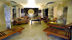 Un espacio de spa con tumbonas de madera, una mesa central con un florero, y un elemento decorativo circular en la pared.