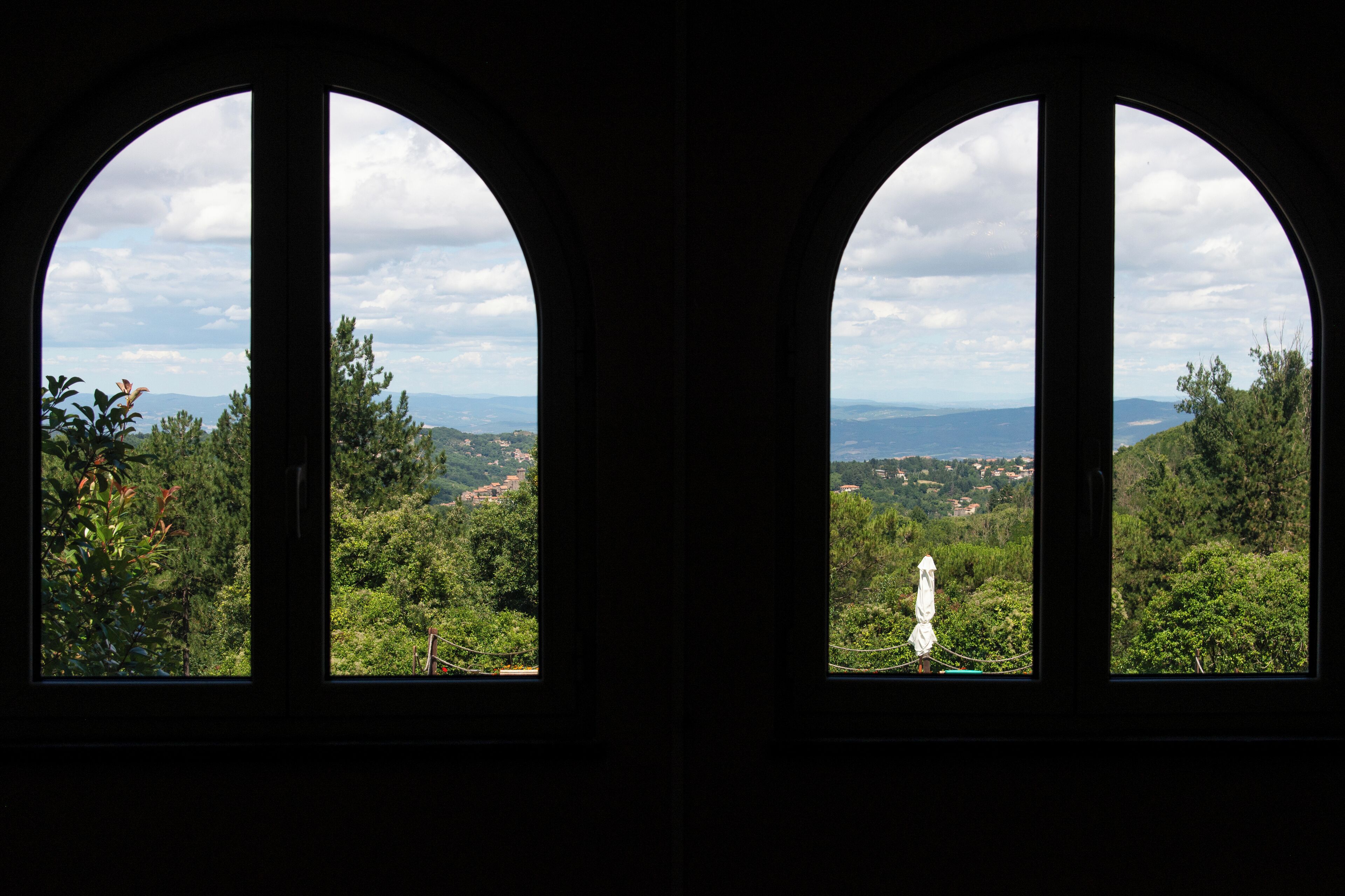 Two arched windows with a view of a mountainous landscape and distant buildings.