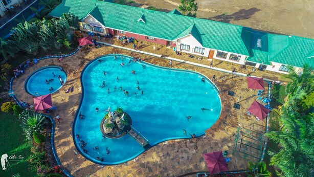 An aerial view of a resort with multiple swimming pools, a central large pool, and a building with a green roof.