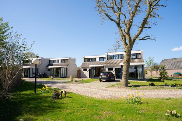 A modern residential area with two-story houses, a paved driveway, and a tree in the foreground. - Holiday home in De Cocksdorp (De Cocksdorp)