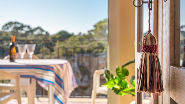 A table with a striped tablecloth, a bottle, and two glasses, with a view of trees and a building in the background. - The Torrent's Observer Holiday Home (Cala Pi) Free wifi, Smart Tv, Satellite (Cala Pi - Llucmajor)
