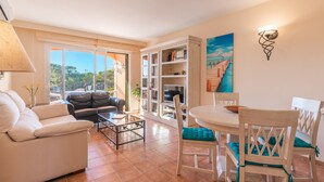 A living room with a sofa, a dining table with chairs, a bookshelf, and a painting on the wall. - The Torrent's Observer Holiday Home (Cala Pi) Free wifi, Smart Tv, Satellite (Cala Pi - Llucmajor)