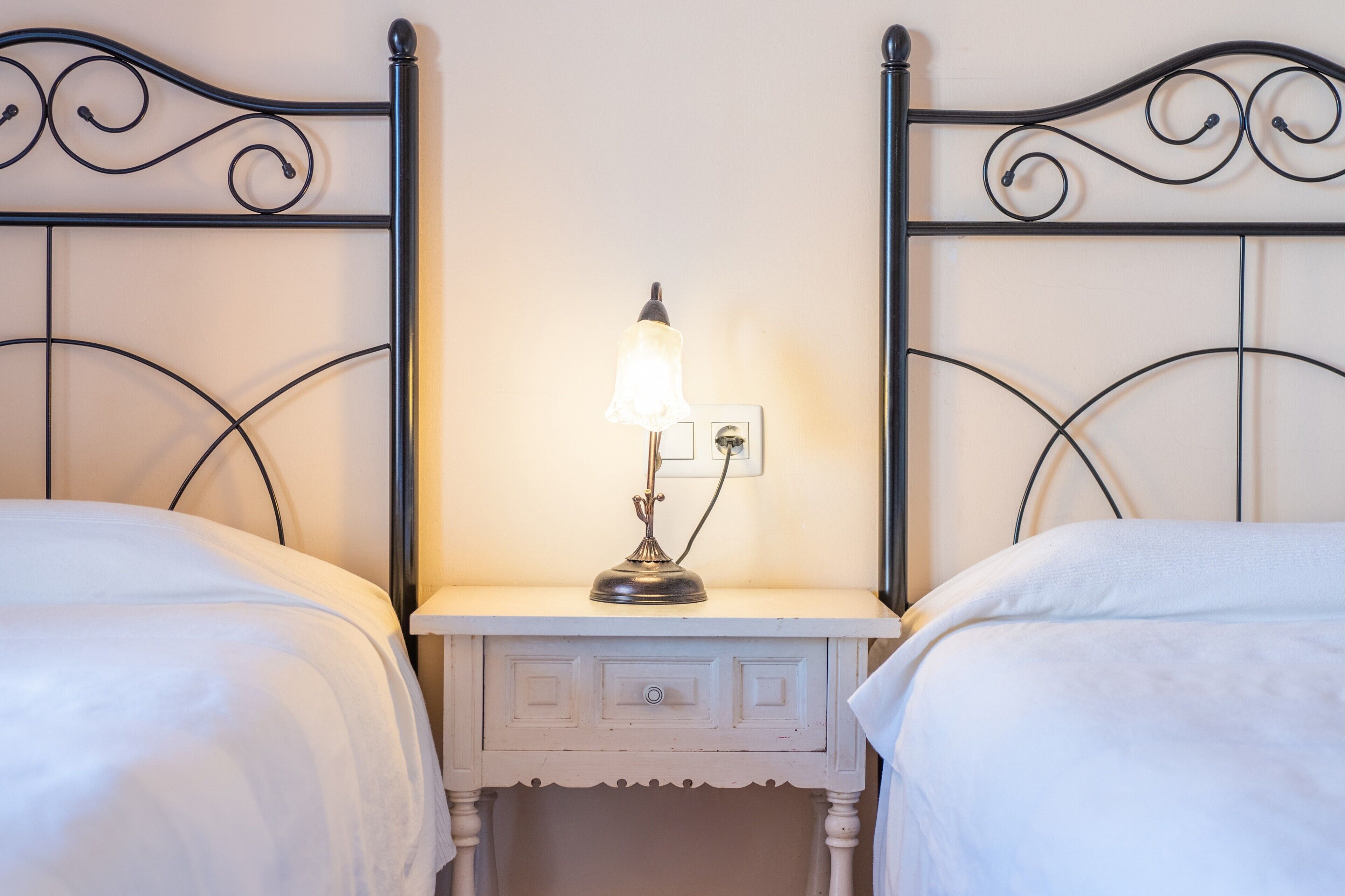 A double bed with white bedding, a bedside table with a lamp, and a wall-mounted light switch.