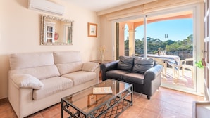 A living room with a beige sofa, a black leather sofa, and a glass coffee table. There is a large mirror on the wall and a window with a view of greenery. - The Torrent's Observer Holiday Home (Cala Pi) Free wifi, Smart Tv, Satellite (Cala Pi - Llucmajor)