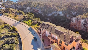 A coastal road with a curve, a building with a tiled roof, and a cliffside with dense vegetation. - The Torrent's Observer Holiday Home (Cala Pi) Free wifi, Smart Tv, Satellite (Cala Pi - Llucmajor)