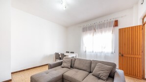 Ein Wohnzimmer mit einer Eckcouch, einem Glastisch, einem Essbereich mit Tisch und Stühlen sowie einer Holztür.