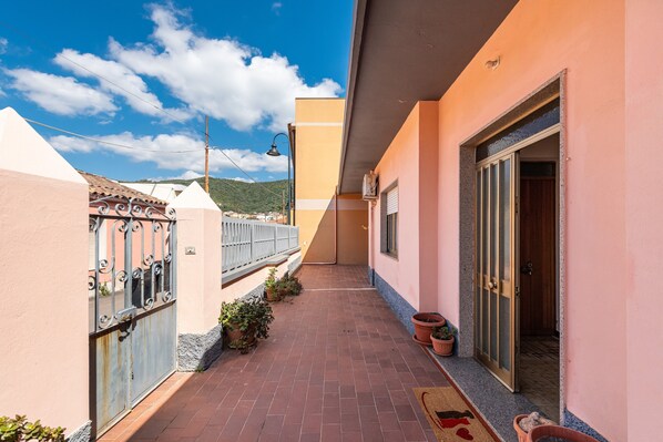 A narrow outdoor corridor with a tiled floor, metal gate, potted plants, and a building entrance.