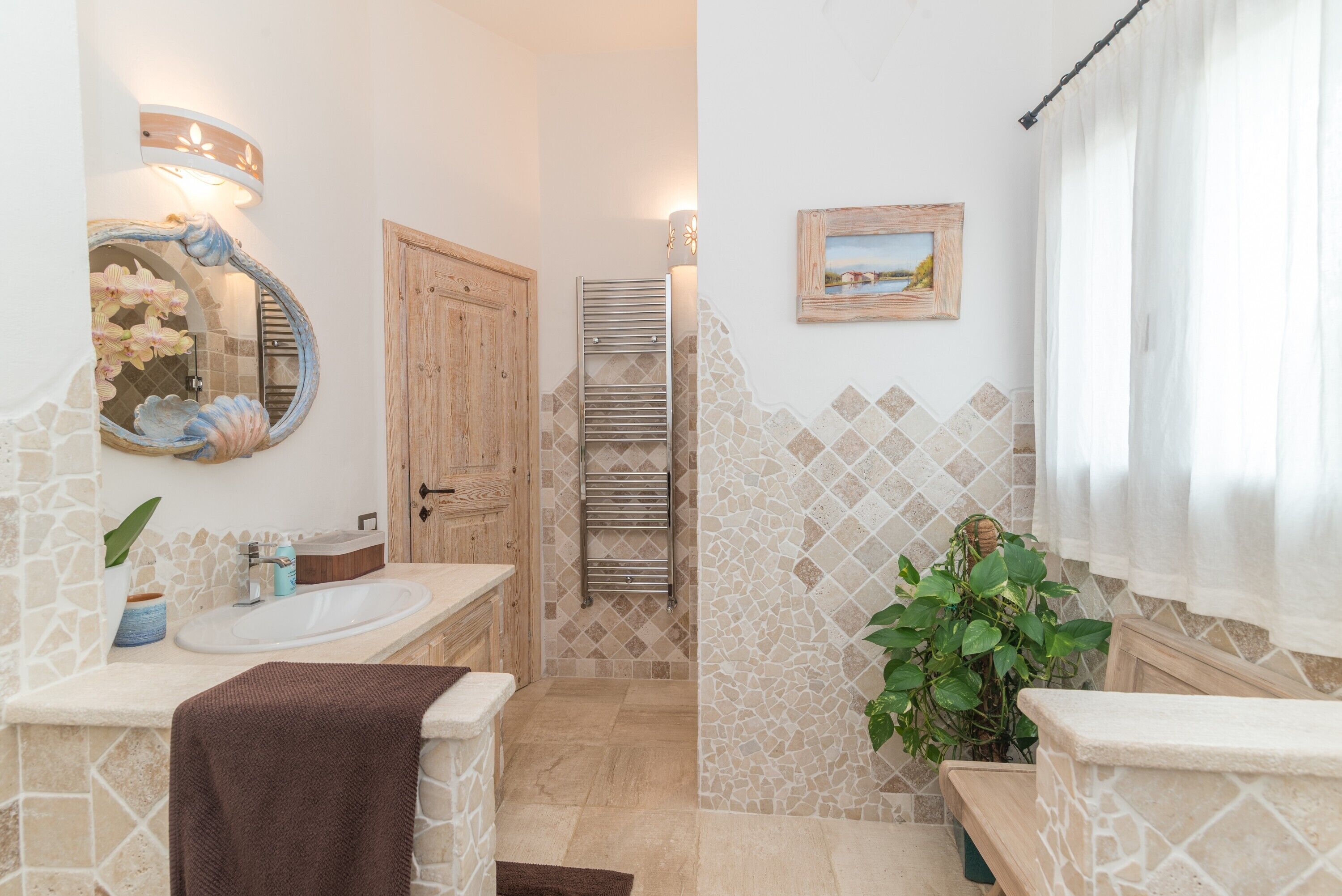 A bathroom with a stone wall, a wooden door, a sink, a mirror, a towel, a potted plant, and a framed picture on the wall.