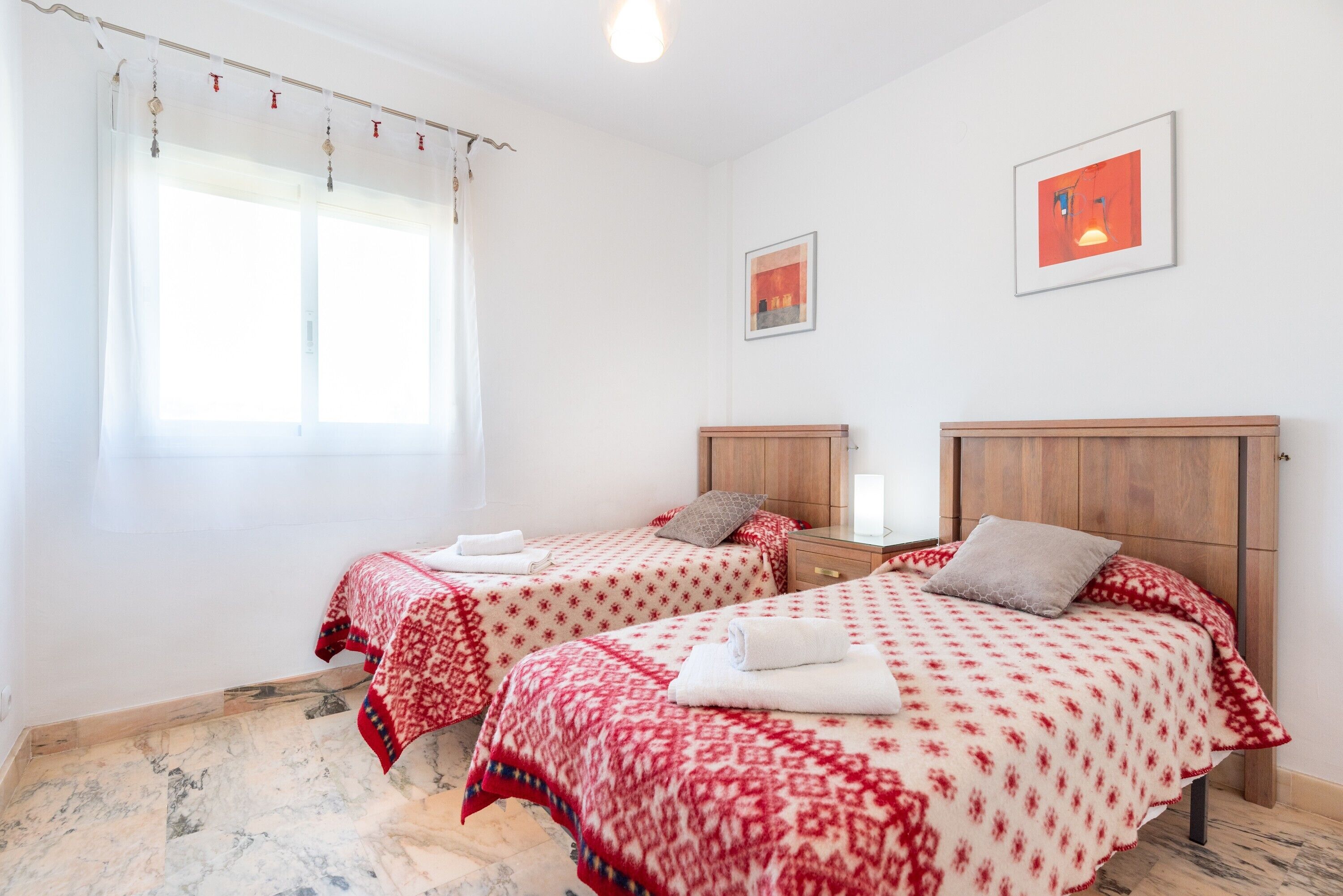 Een kamer met twee bedden, een houten hoofdbord, een raam met gordijnen en een ingelijste foto aan de muur.