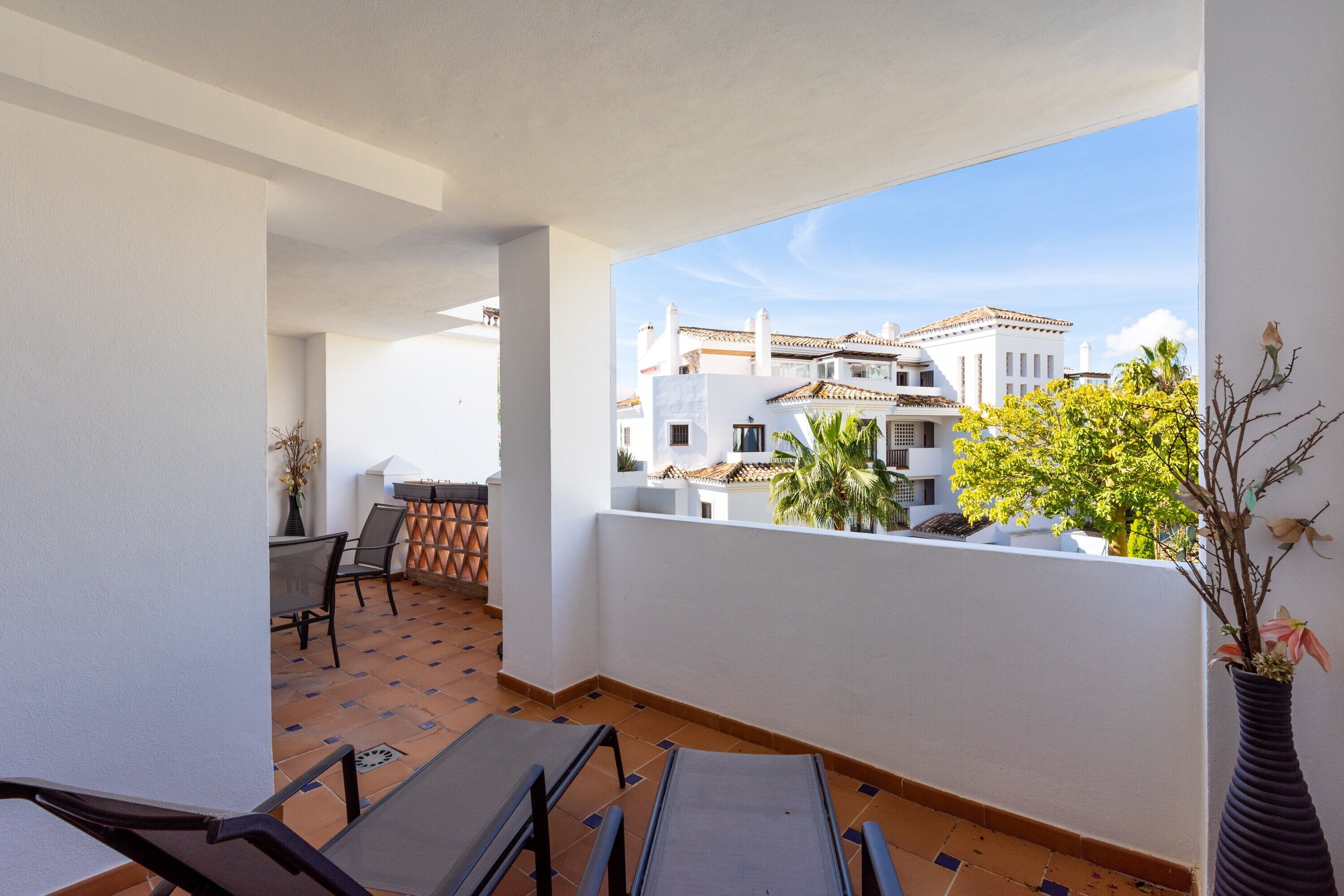 A balcony with a view of traditional buildings, a table with chairs, and a potted plant.