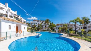 A swimming pool with a curved edge, surrounded by a fence and palm trees. - Apartment "Finca San Antonio Holiday Rental" with Pool, Terrace & Wi-Fi (Mijas Pueblo)