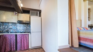 A compact kitchen with a refrigerator, microwave, and tiled backsplash. - Studio 'Sa Burrida' Relax close to the Sea with Garden & Wi-Fi (Posada)