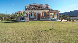 A two-story house with a stone facade, a balcony, and a thatched roof structure. - Studio 'Sa Burrida' Relax close to the Sea with Garden & Wi-Fi (Posada)