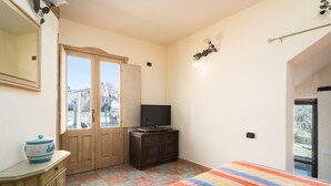 A bedroom with a bed, a television on a wooden cabinet, a large window, and a door leading outside. - Studio 'Sa Burrida' Relax close to the Sea with Garden & Wi-Fi (Posada)