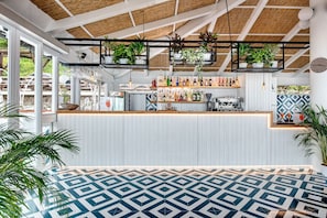 A modern bar area with a white counter, hanging plants, and a patterned floor. - Blue-wave Experience Resort (Massa Lubrense)