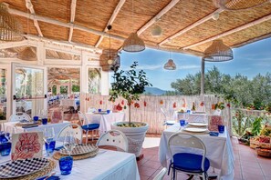 An outdoor dining area with tables set for guests, a large potted plant, and a view of the surrounding landscape. - Blue-wave Experience Resort (Massa Lubrense)