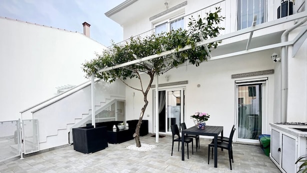 Un patio con una mesa y sillas, una escalera blanca y un árbol.