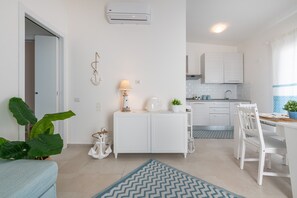 A modern kitchen with white cabinets, a dining area with a table and chairs, and a living area with a sofa and a plant. - Pet-Friendly Apartment 'La Casa dei Naviganti' with Courtyard and Wi-Fi (Villasimius)