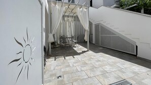 A covered outdoor patio with a table and chairs, a staircase, and a white building in the background. - Pet-Friendly Apartment 'La Casa dei Naviganti' with Courtyard and Wi-Fi (Villasimius)