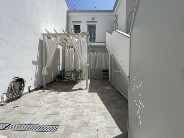 Ein Innenhof mit einer Pergola, einem Tisch, Stühlen und einem kleinen Hocker.