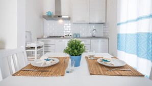 A modern kitchen with white cabinets, a blue pot with a plant, and a dining table set with plates and cutlery. - Pet-Friendly Apartment 'La Casa dei Naviganti' with Courtyard and Wi-Fi (Villasimius)