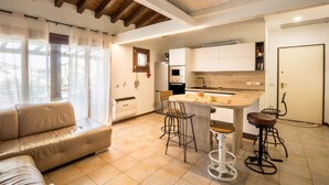 Een moderne keuken met een centraal eiland, barstoelen en een bank in een lichte woonkamer met grote ramen.