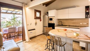Een moderne keuken met een houten keukeneiland, een eetgedeelte met een tafel en stoelen, en uitzicht op een balkon met buitenmeubilair.