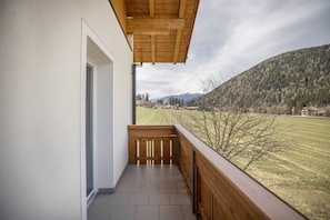 Ein Balkon mit Holzwertung, Blick auf ein grünes Feld und ein Berg in der Ferne.
