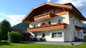 A multi-story building with wooden balconies, a covered patio, and a mountainous backdrop. - Apartment 'Unterhauserhof B' with Mountain View, Wi-Fi, Balcony & Garden (Mitterolang)