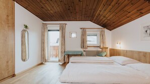 A room with a wooden ceiling, a bed with white bedding, a small table with a green tablecloth, and a window with curtains. - Apartment 'Unterhauserhof B' with Mountain View, Wi-Fi, Balcony & Garden (Mitterolang)