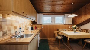 A kitchen with wooden cabinets, a sink, a dining table with chairs, and a window with curtains. - Apartment 'Unterhauserhof B' with Mountain View, Wi-Fi, Balcony & Garden (Mitterolang)