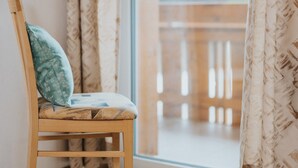 A wooden chair with a cushion, positioned next to a window with patterned curtains. - Apartment 'Unterhauserhof B' with Mountain View, Wi-Fi, Balcony & Garden (Mitterolang)
