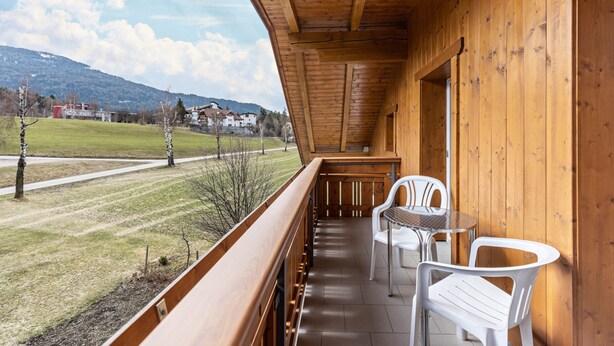 A wooden balcony with a view of a grassy field and houses in the distance. - Apartment 'Unterhauserhof B' with Mountain View, Wi-Fi, Balcony & Garden (Mitterolang)