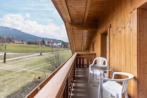 Een houten balkon met uitzicht op een grasveld en huizen in de verte.