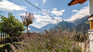 Un paysage montagneux avec une clôture en bois, un bâtiment blanc doté d’une porte jaune et un ciel dégagé.