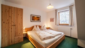 Une chambre à coucher avec un lit en bois, une table de chevet, une armoire, un tableau encadré au mur et une fenêtre avec des rideaux.